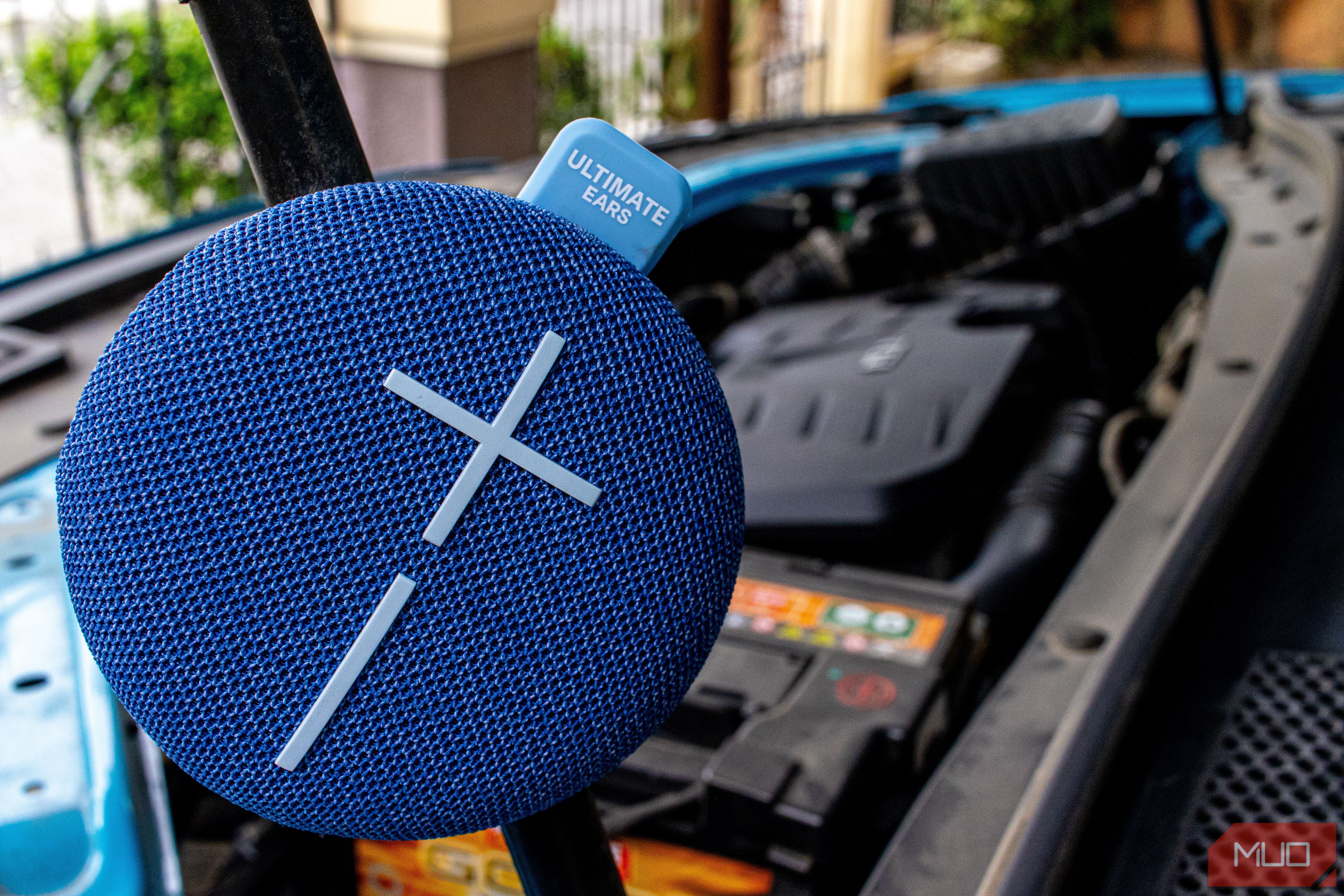 Ultimate Ears Miniroll attached to the hood strut of a car.