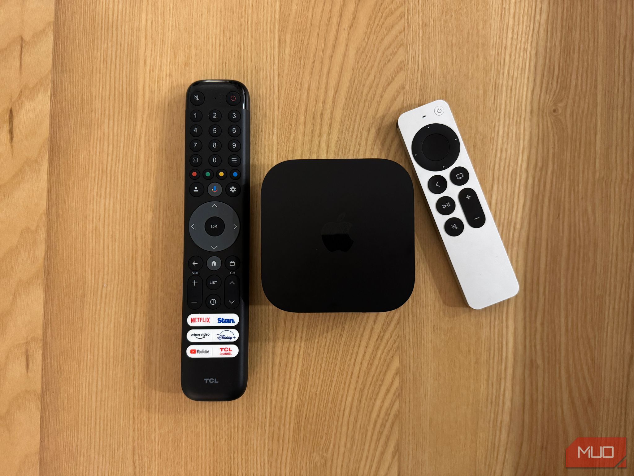 An Apple TV, a Siri Remote, and a TCL TV remote placed on a table.