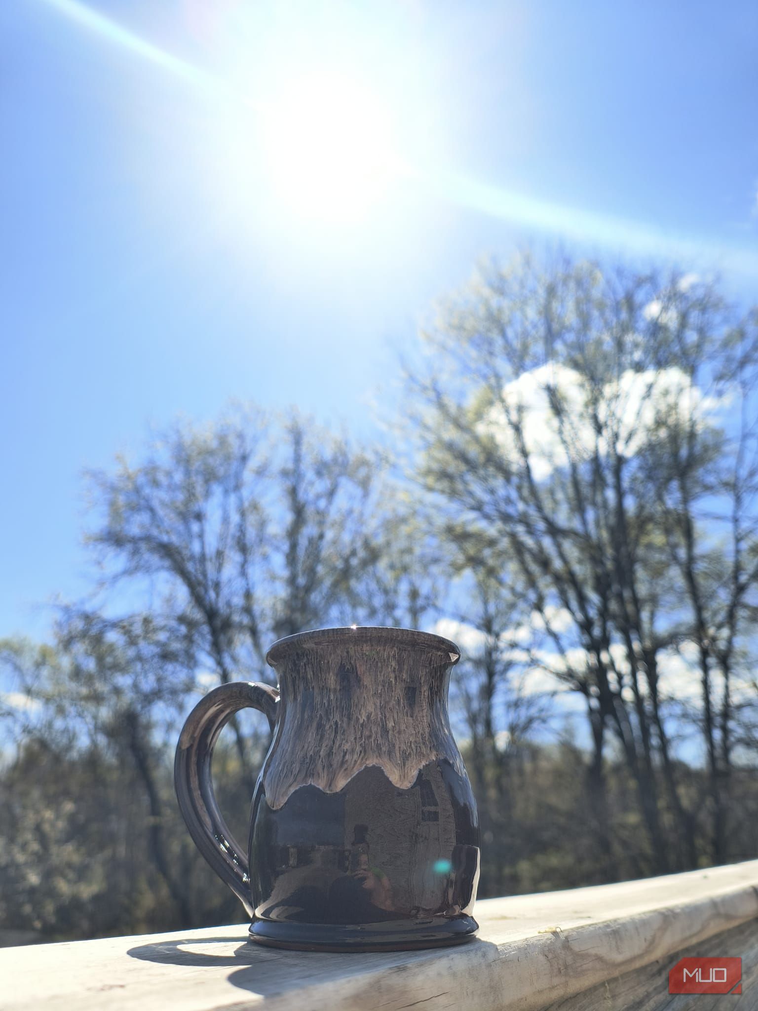 A mug on a wooden hand rail with the sun and blue sky behind it—HDR disabled
