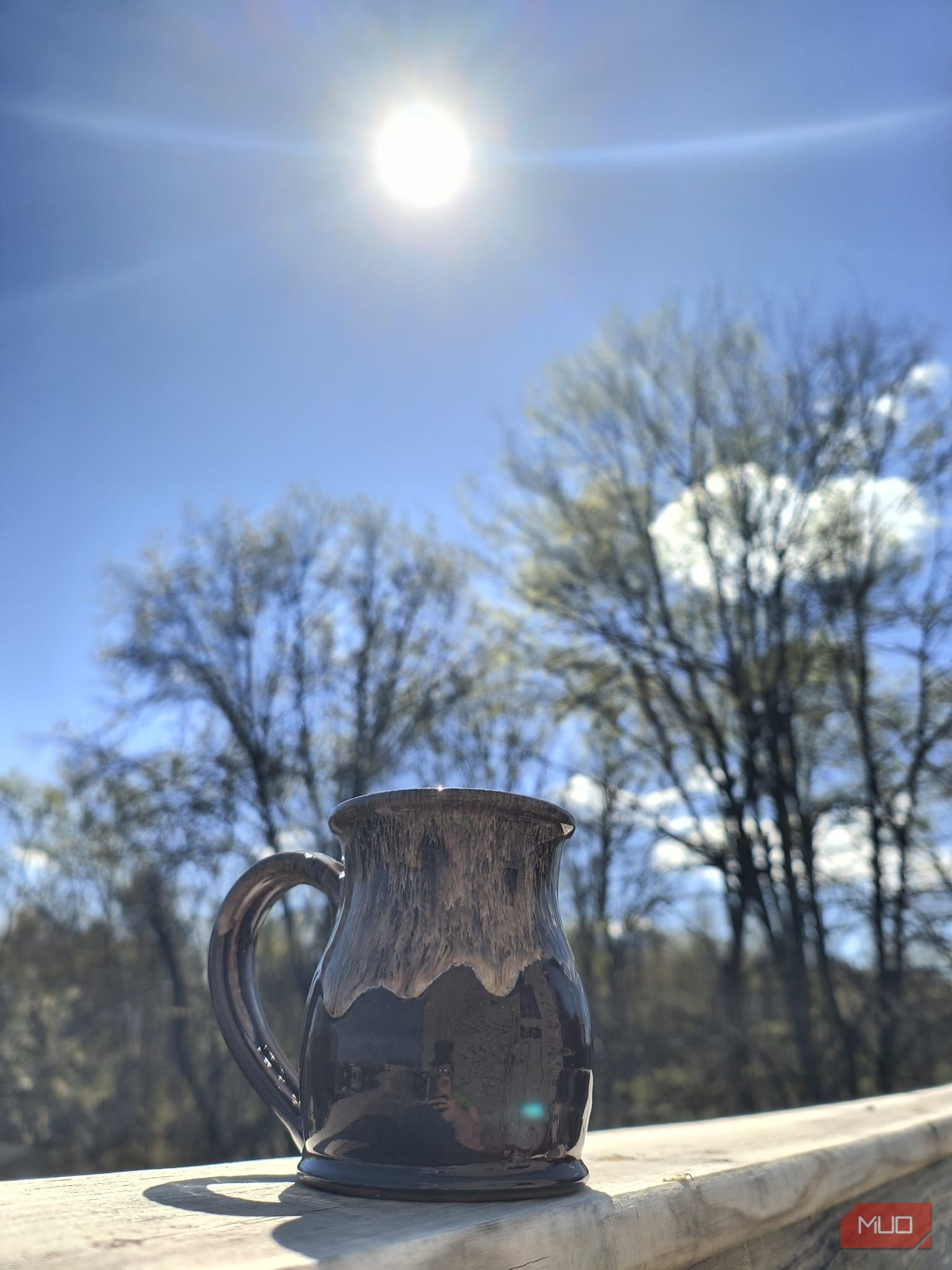 A mug on a wooden hand rail with the sun and blue sky behind it—HDR enabled