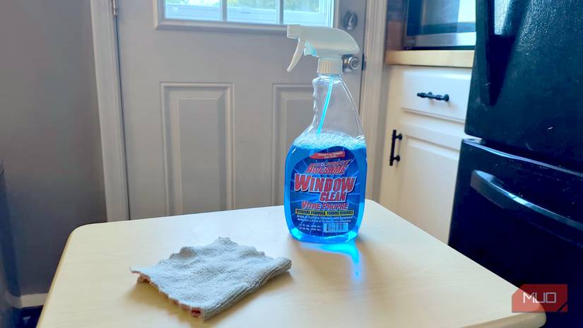 A bottle of window washing solution next to a microfiber cloth on a small table
